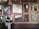 A person stands in front of a gallery wall filled with framed paintings of various sizes. The artworks depict a variety of scenes, including landscapes, a crucifixion, and mythological settings. The wall is painted pink, and the space has a classic, museum-like feel.