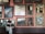 A person stands in front of a gallery wall filled with framed paintings of various sizes. The artworks depict a variety of scenes, including landscapes, a crucifixion, and mythological settings. The wall is painted pink, and the space has a classic, museum-like feel.