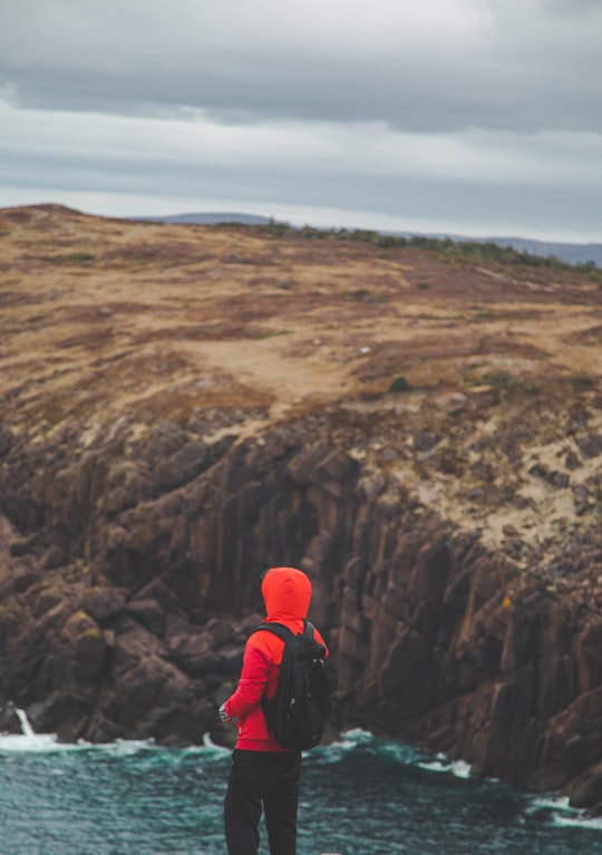 person in red jacket and black pants with red backpack standing on rocky mountain during daytime in Cape Spear Canada