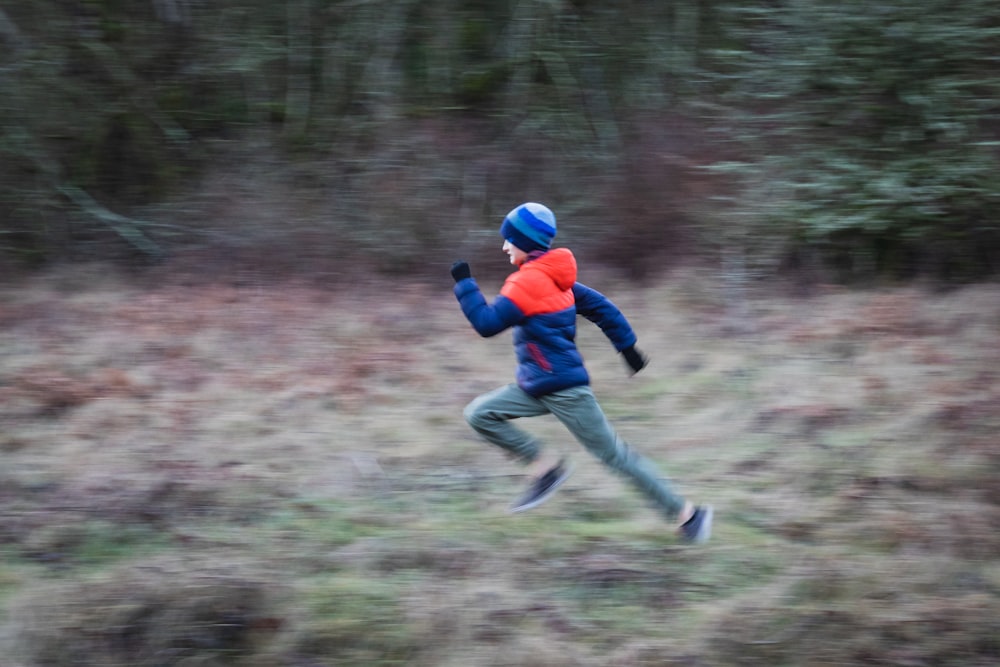 boy in red jacket and blue denim jeans jumping on green grass field during daytime