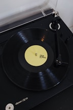 A vinyl record player with a rotating black vinyl disc featuring a yellow label. The label reads 'COEUR DE PIRATE FACE A'. The turntable arm is positioned over the record, and the player itself appears to be sleek and modern in design.
