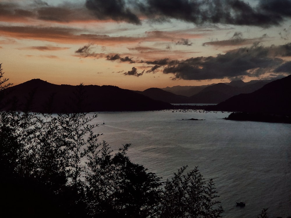 body of water near mountain under cloudy sky during daytime