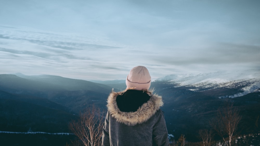 person in brown and black parka jacket and gray knit cap standing on green grass field