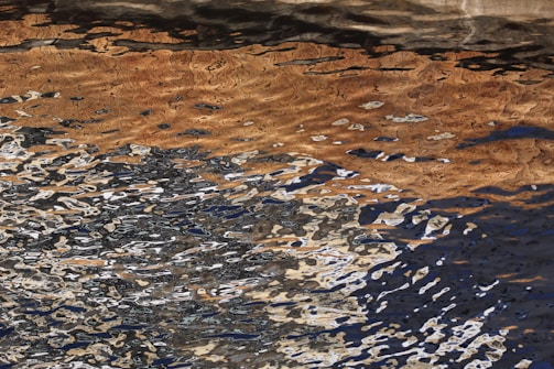 A chaotic interplay of reflected light creates an abstract pattern on the surface of water. The image captures the distortion of various colors, including brown, black, and white, in wavy motion.