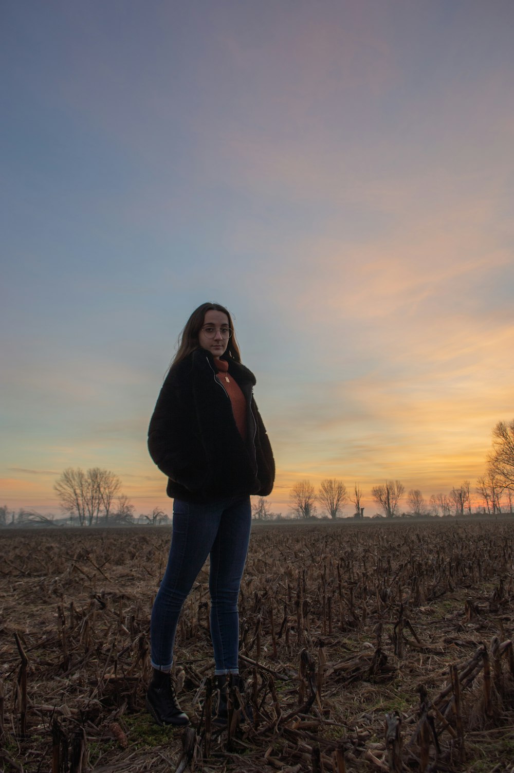 Frau in schwarzer Jacke und blauen Jeans tagsüber auf braunem Feld