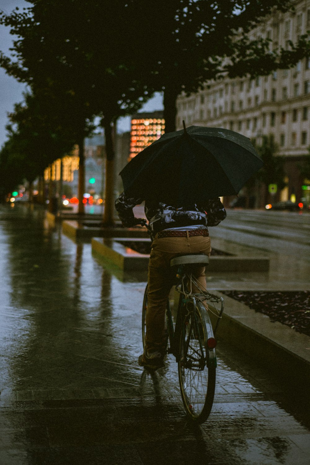 person in black jacket and blue denim jeans holding umbrella walking on sidewalk during daytime