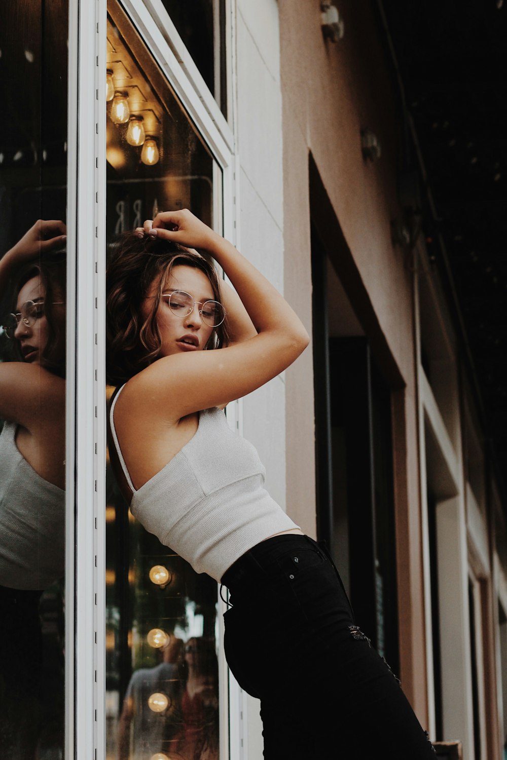 woman in white tank top and black pants standing beside glass window