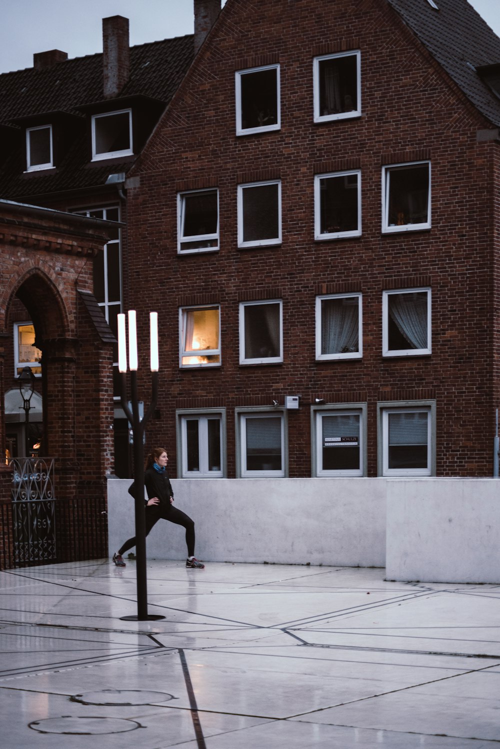 woman in black coat walking on sidewalk near brown building during daytime