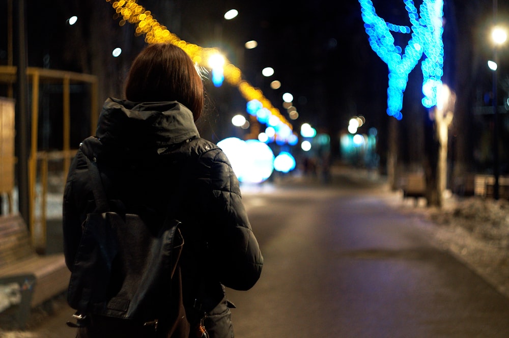 woman in black jacket standing on sidewalk during night time