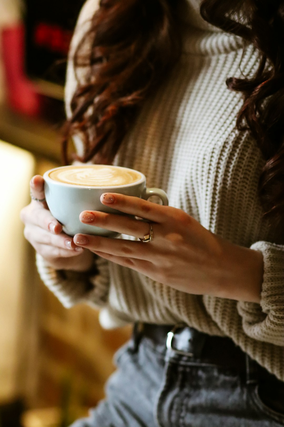 woman in gray sweater holding white ceramic mug