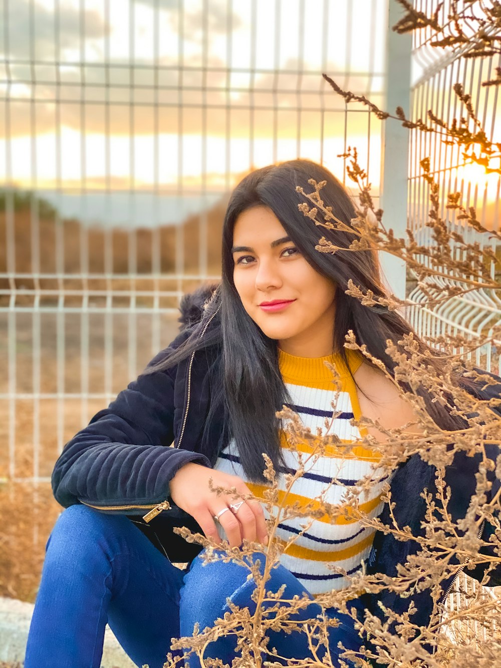 woman in black jacket and blue denim jeans sitting on brown dried leaves