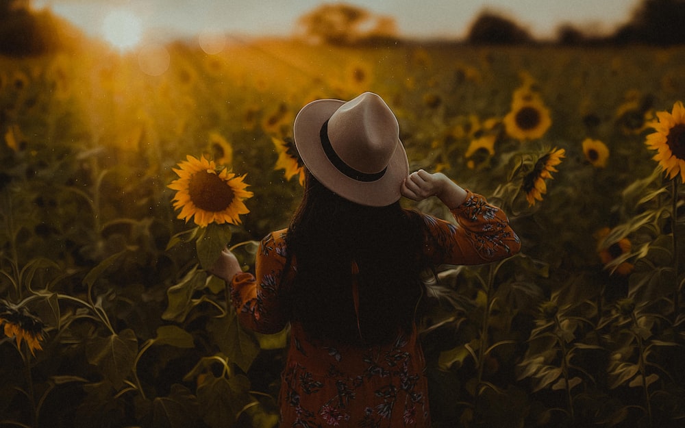 woman in black and red floral dress wearing white fedora hat standing on sunflower field during
