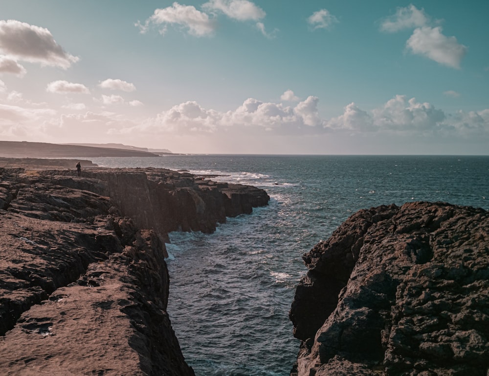 brown rocky mountain beside blue sea under blue and white cloudy sky during daytime