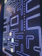 A close-up view of a retro arcade game screen featuring a classic maze with blue neon-like outlines and dotted paths. The game elements include iconic dots and corridors typical of vintage gaming interfaces.