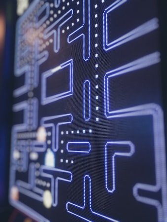 A close-up view of a retro arcade game screen featuring a classic maze with blue neon-like outlines and dotted paths. The game elements include iconic dots and corridors typical of vintage gaming interfaces.