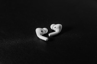 Two white wireless earbuds are placed on a dark, textured surface. They are positioned next to each other, showcasing their ergonomic design.