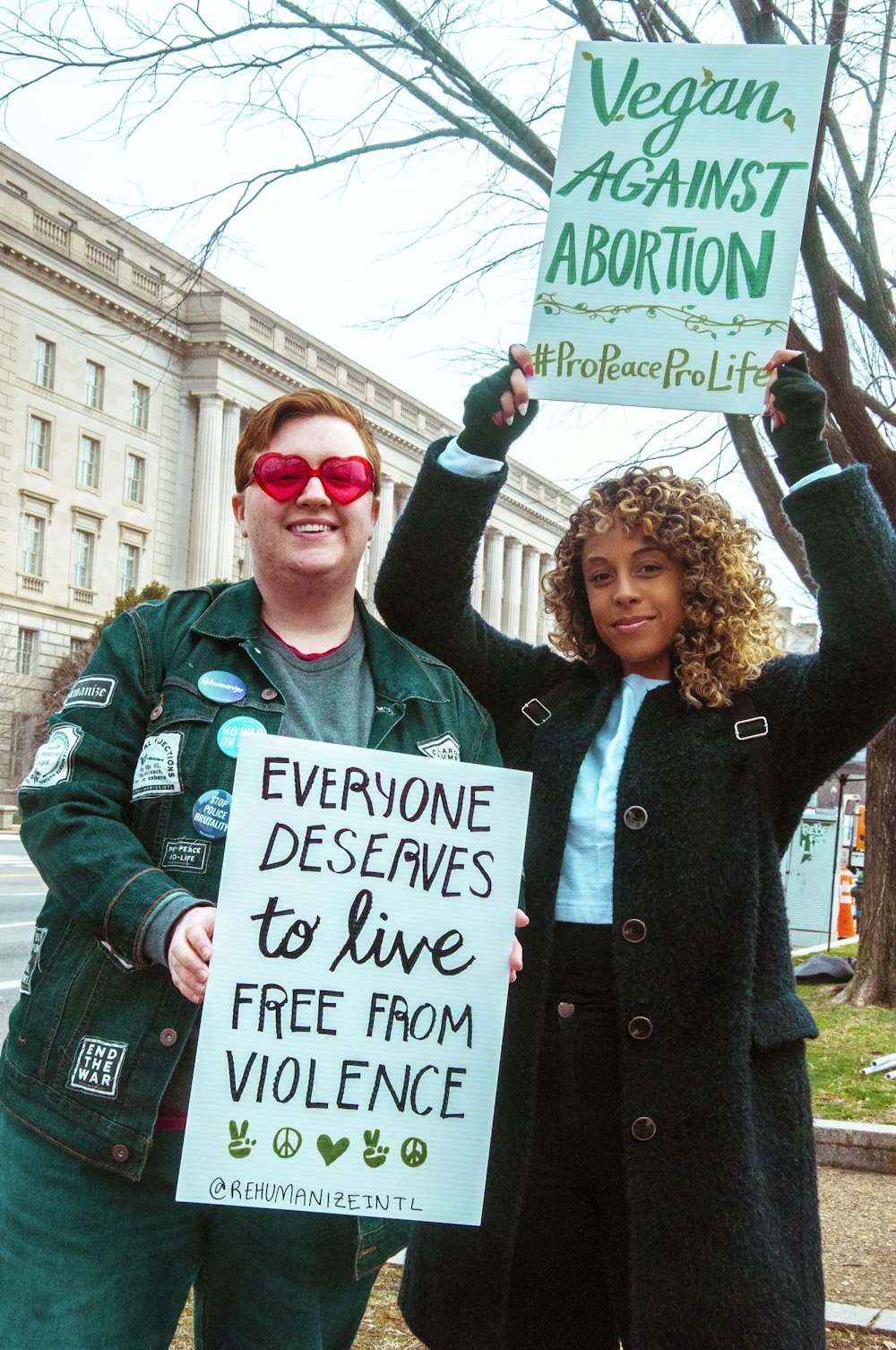 A pro-life on the left holding a sign that says: "Everyone deserves to live free from violence." And another woman holding up a sign "Vegan against abortion #ProPeaceProLife"