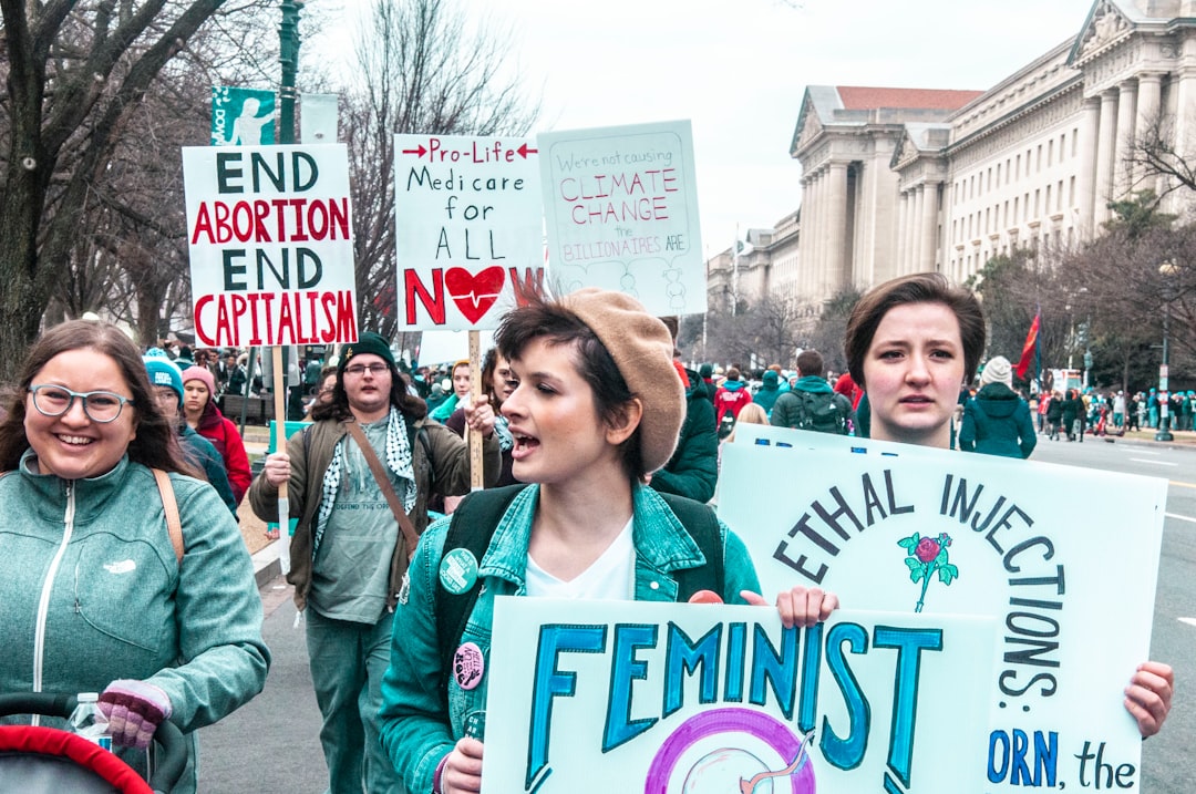 woman in green jacket standing beside woman in green jacket holding white and pink signage