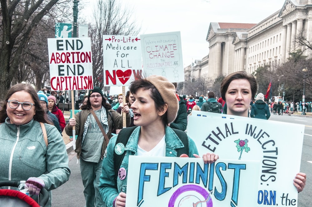 woman in green jacket standing beside woman in green jacket holding white and pink signage