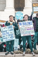 A group of people participating in a protest, holding signs advocating for pro-choice and other social justice causes. The scene is set on the steps of a governmental building, possibly a courthouse. The people are wearing warm clothing, suggesting it's a cooler day.