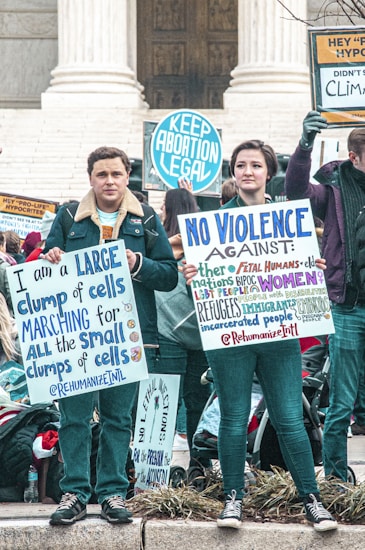 A group of people participating in a protest, holding signs advocating for pro-choice and other social justice causes. The scene is set on the steps of a governmental building, possibly a courthouse. The people are wearing warm clothing, suggesting it's a cooler day.