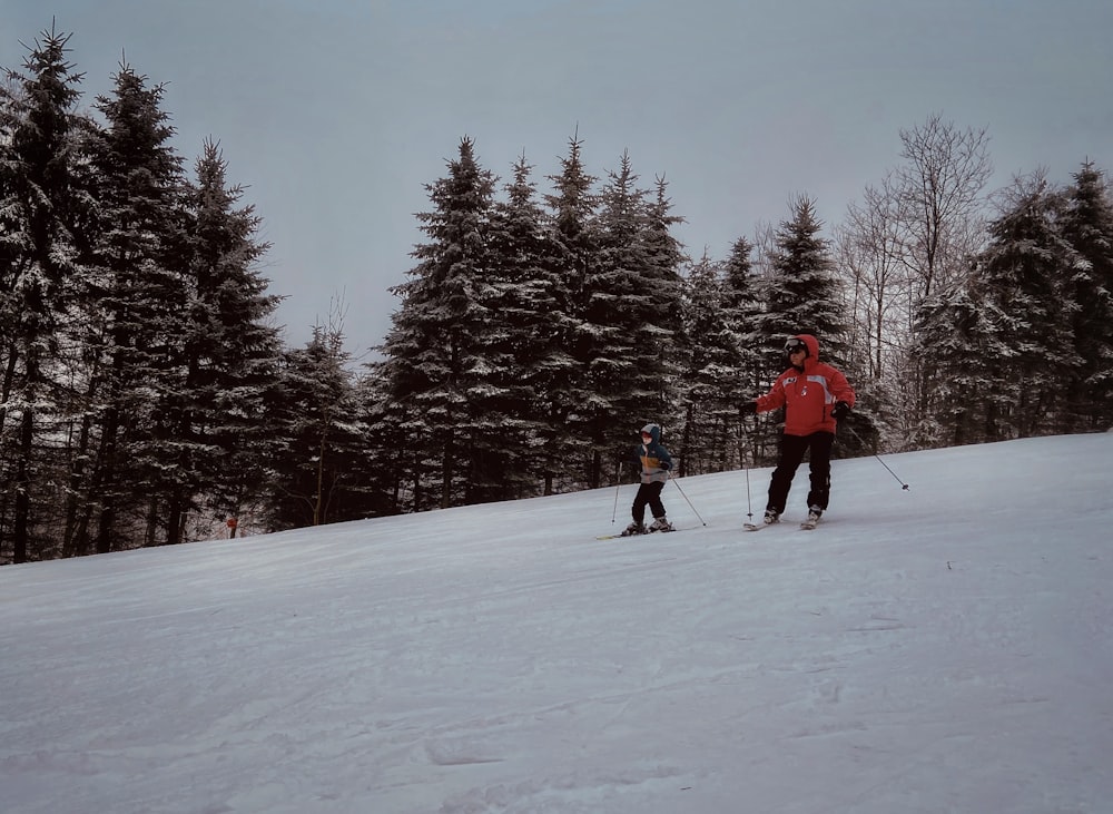 a couple of people riding skis down a snow covered slope