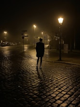 a man walking down a cobblestone street at night