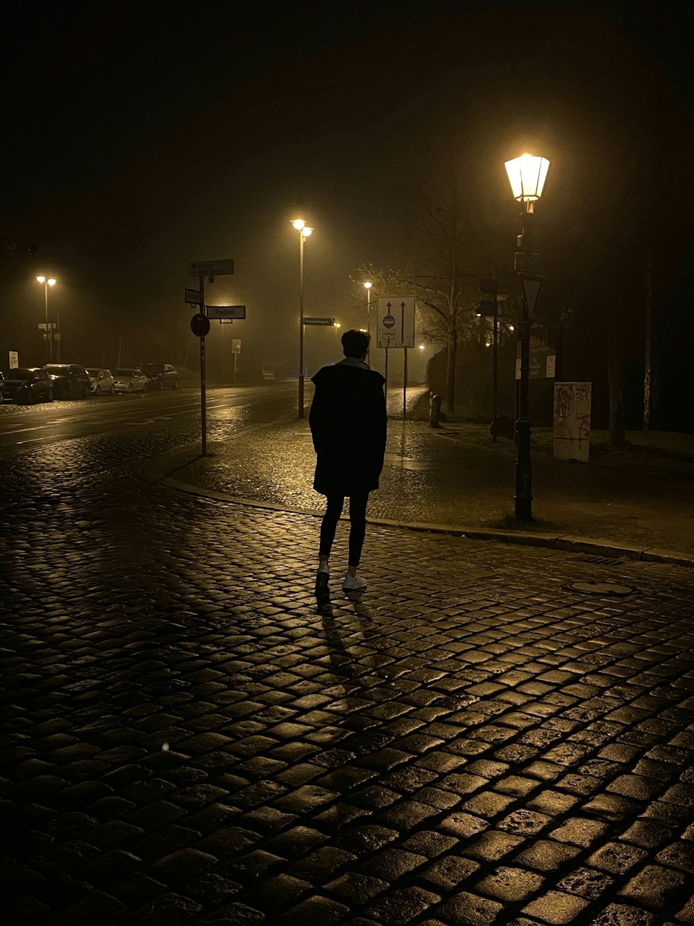 a man walking down a cobblestone street at night