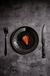 a plate with a strawberry on it next to a knife and fork