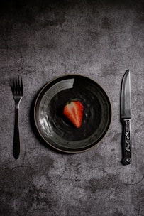 a plate with a strawberry on it next to a knife and fork