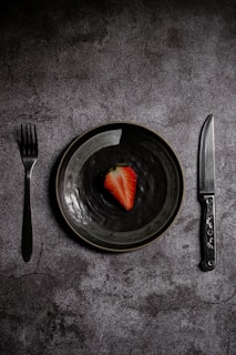 a plate with a strawberry on it next to a knife and fork