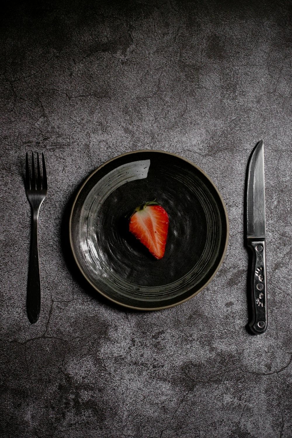 a plate with a strawberry on it next to a knife and fork