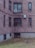 A brick apartment building with several windows, some having bars and others an air conditioning unit. The lower part of the building features basement windows with protective grates. In the courtyard area, a few pigeons are pecking at the sparse grass and fallen leaves.