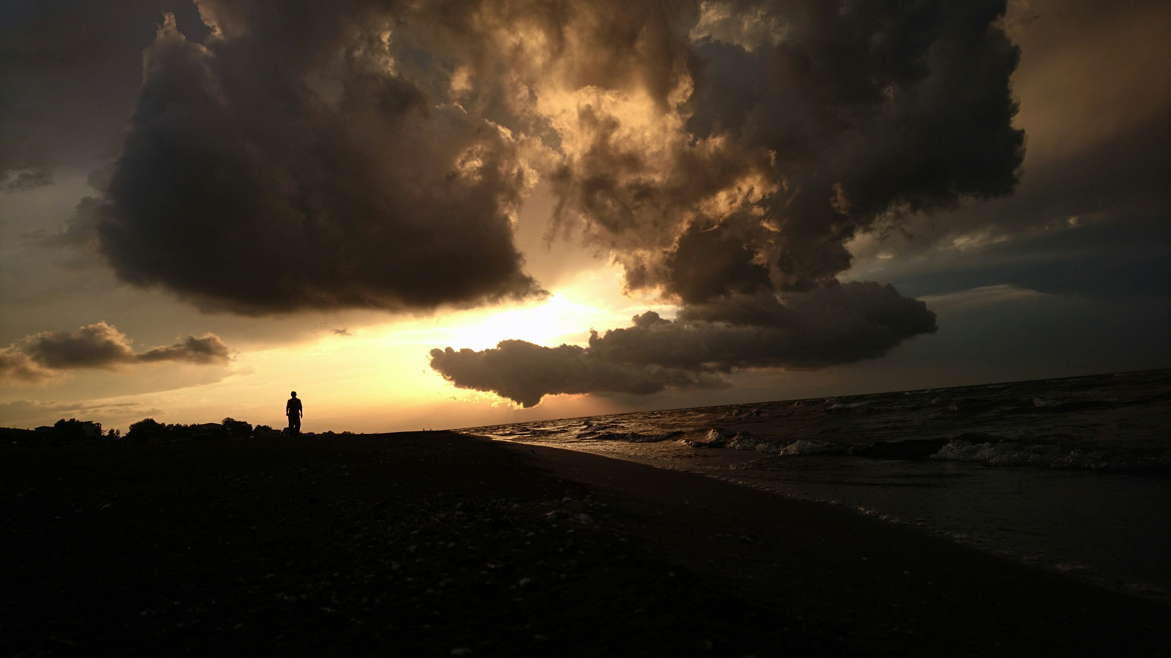 silhouette of person standing on seashore during sunset