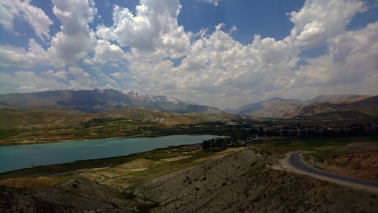 green grass field near body of water under blue and white cloudy sky during daytime in Firouzkouh Iran