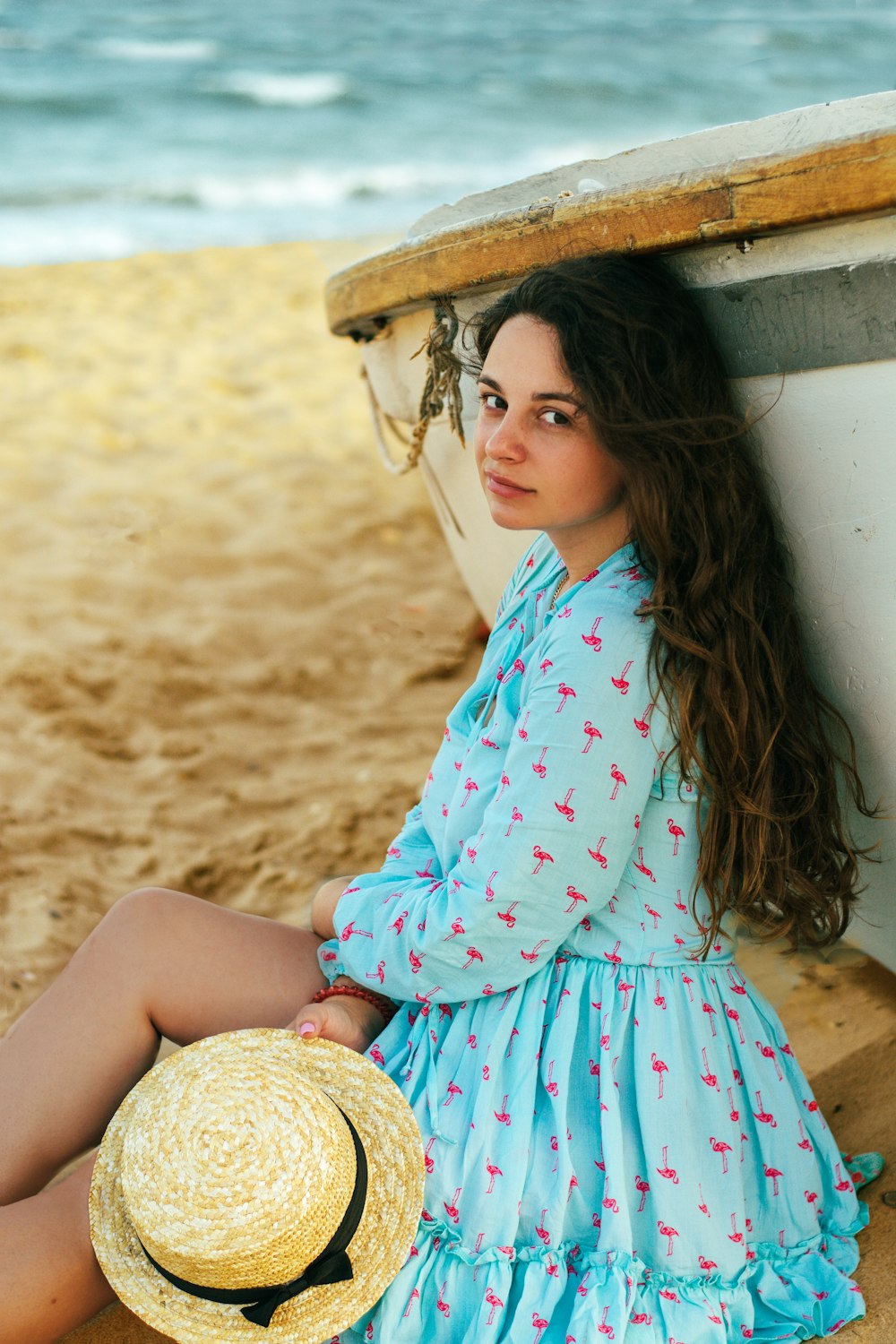 a woman sitting on the beach next to a boat