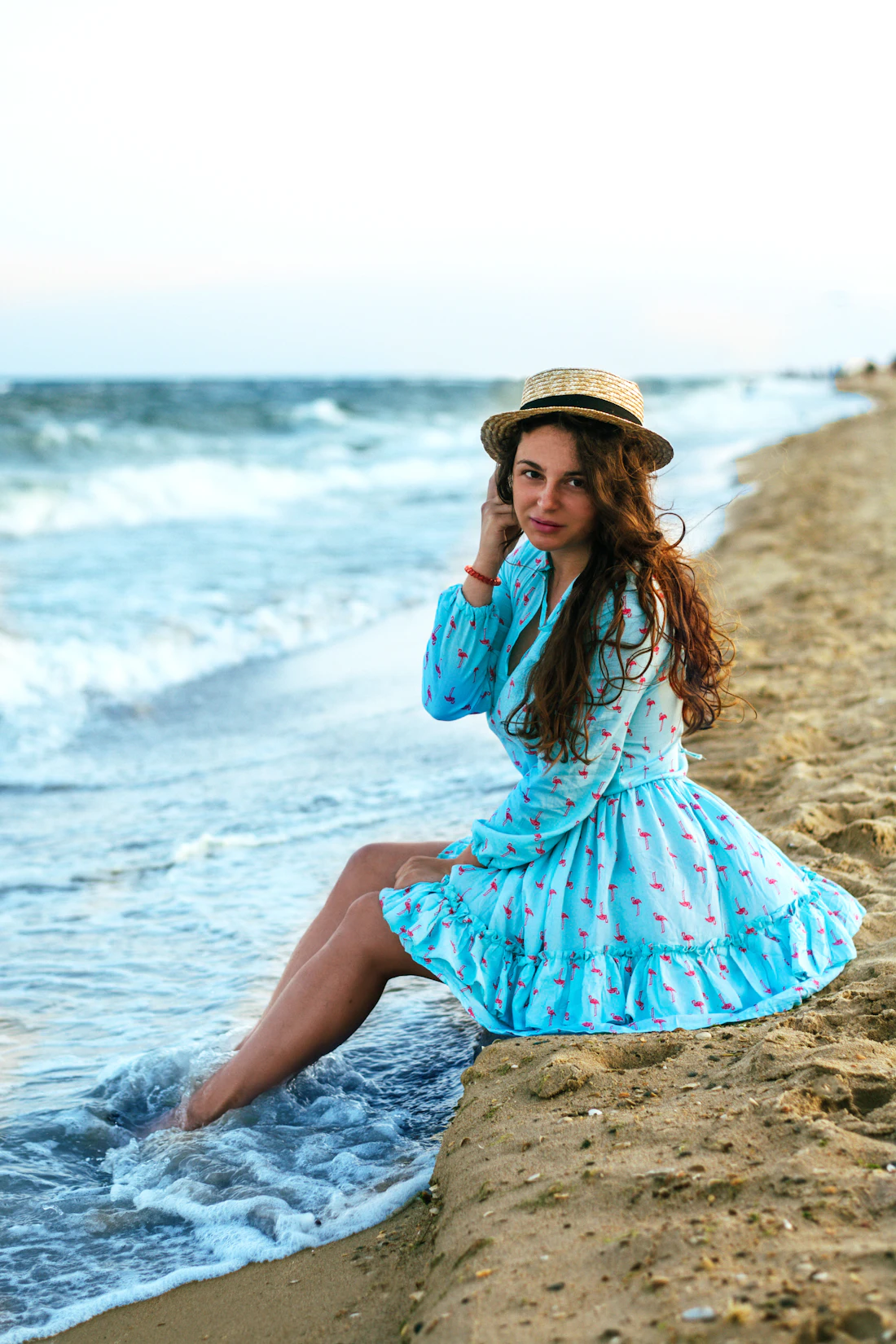 Model in a turquoise flamingo-print ruffle dress at the water's edge