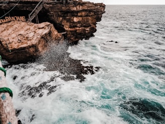 a rocky cliff next to the ocean with a rope