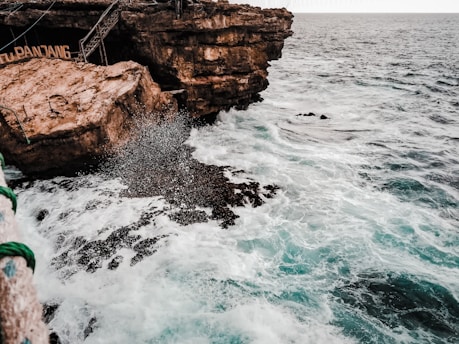 a rocky cliff next to the ocean with a rope
