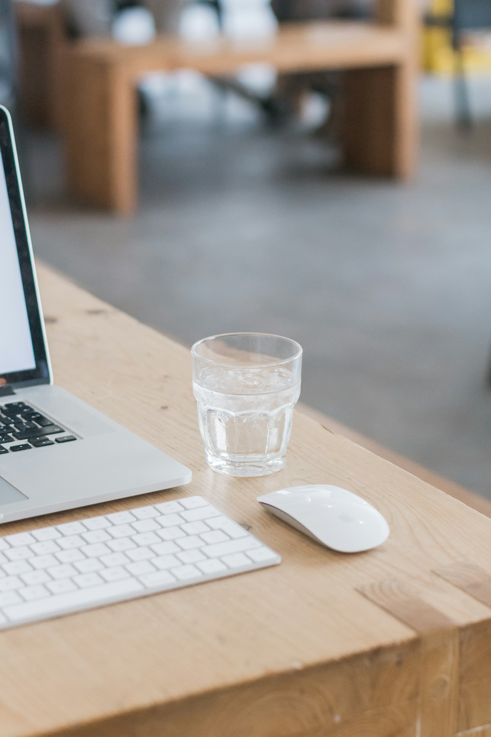 MacBook Pro à côté d’un verre transparent sur une table en bois marron