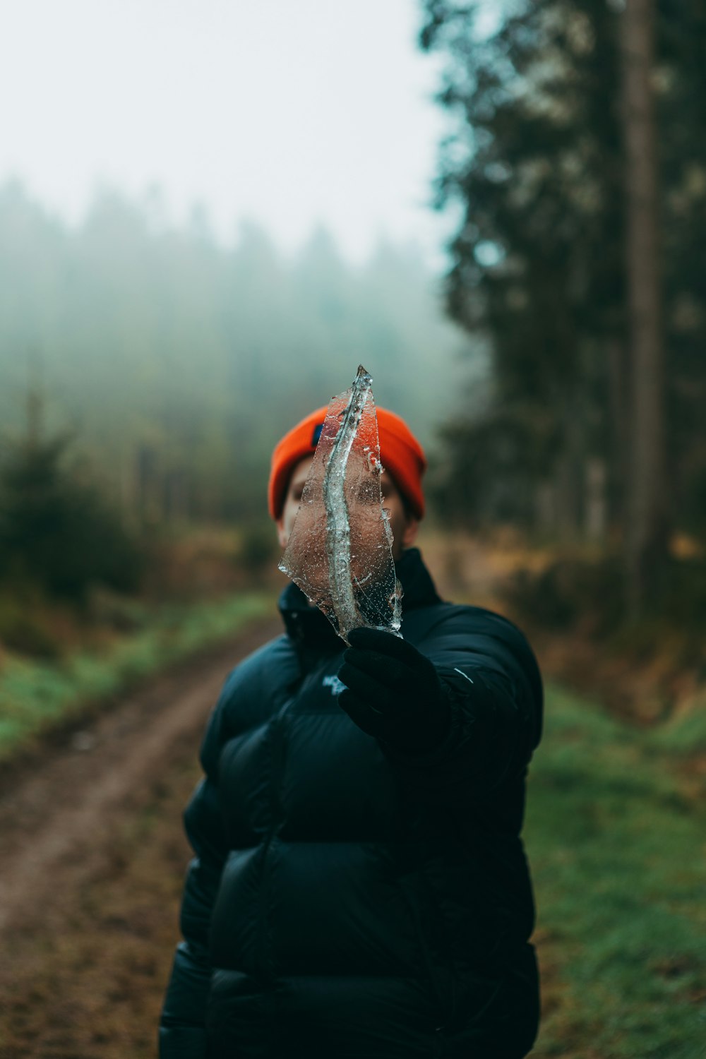 person in black jacket and orange knit cap standing on dirt road during daytime