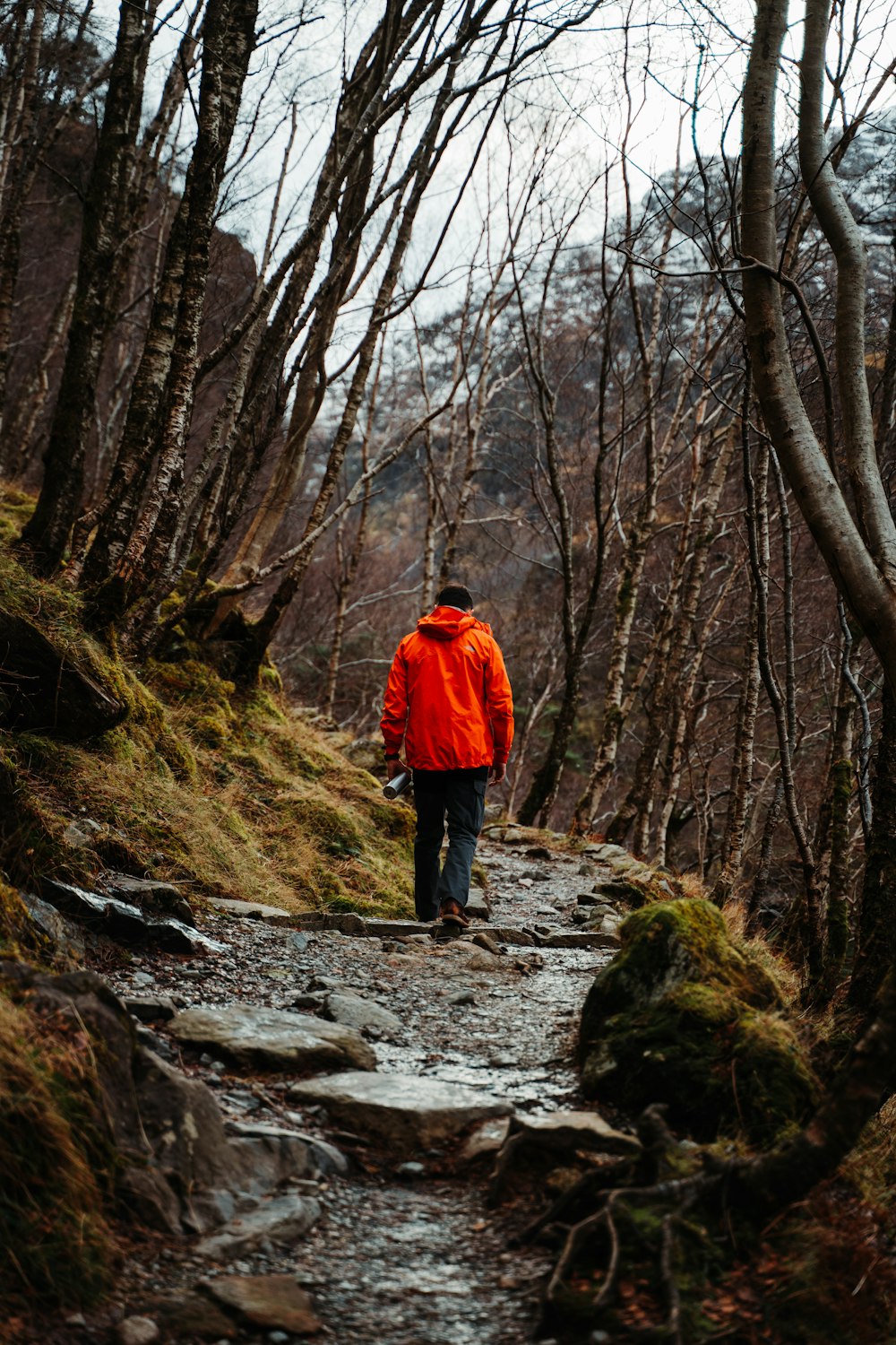 um homem de jaqueta laranja caminhando por uma trilha