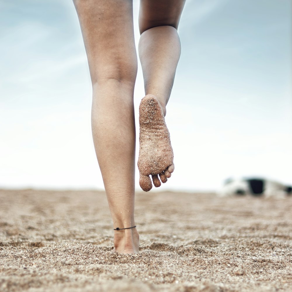 Femme en bas bruns et bottes brunes debout sur le sable brun pendant la journée