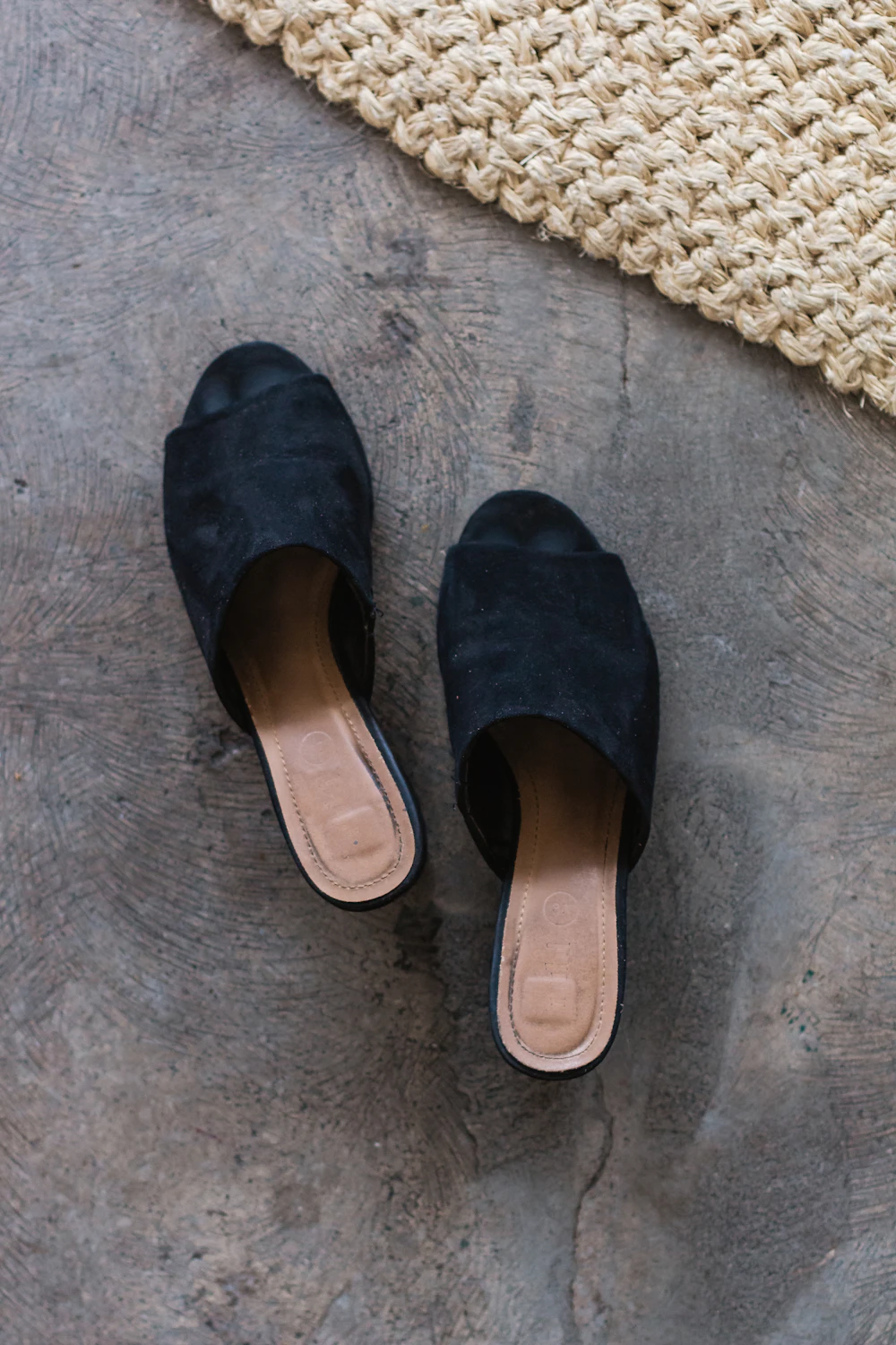 Black suede flat mules on a woven mat