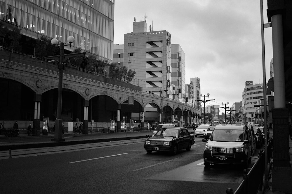 grayscale photo of cars on road near city buildings