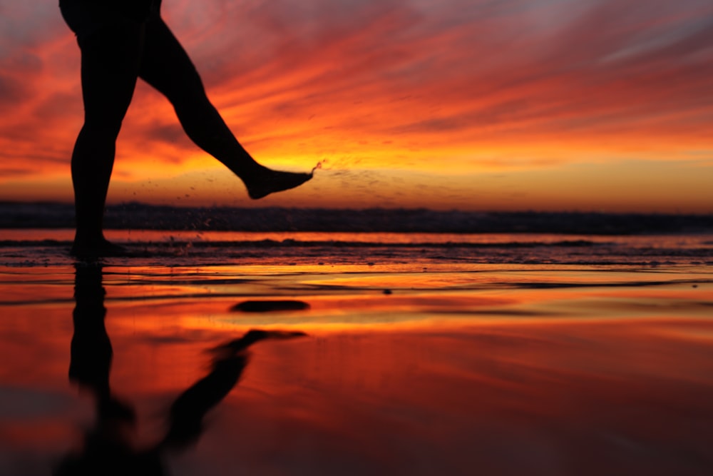 silhouette of person jumping on beach during sunset