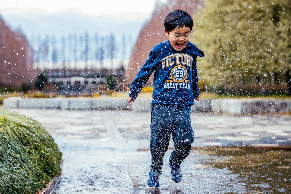 boy in blue and red hoodie standing on wet road during daytime