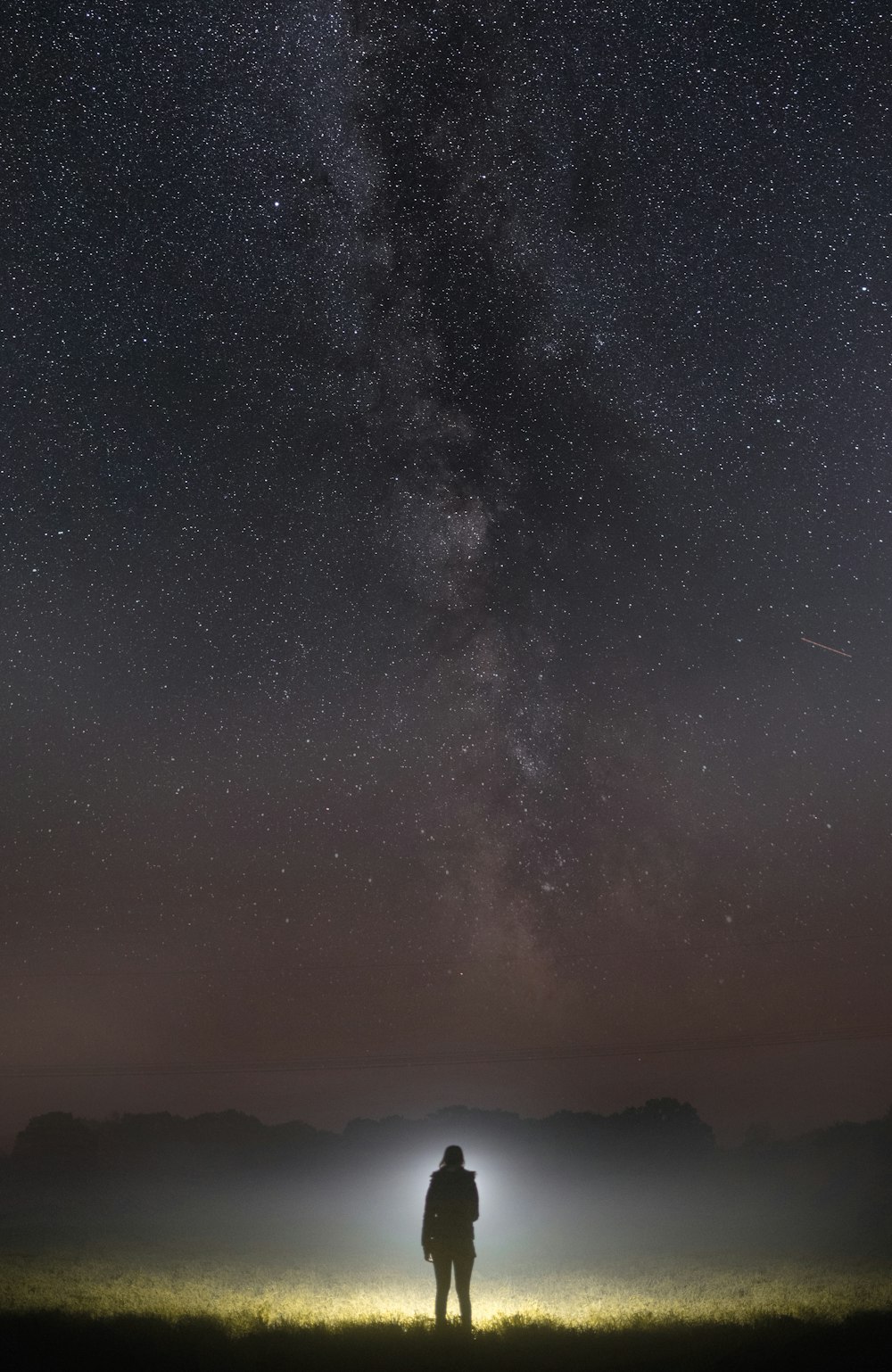 um homem em pé em um campo sob um céu noturno cheio de estrelas