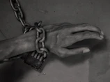 A shadowed figure bound in chains, symbolizing the pain of dehumanization.