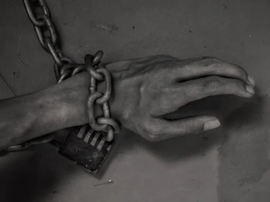 Close-up of hands breaking free from chains under a bright light.